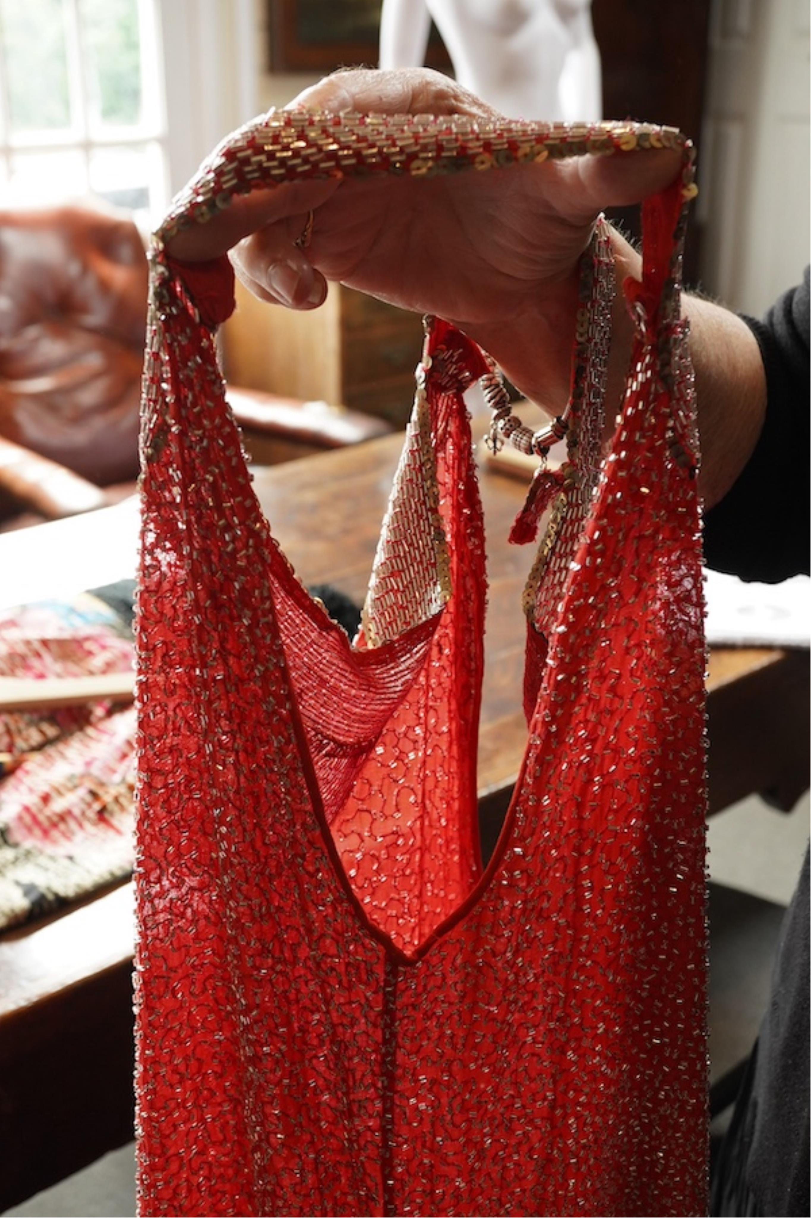A 1920's red georgette beaded evening dress. Hand beaded and sequinned in white and gold, designed with a dropped waist, handkerchief points and wide beaded border with large stylistic floral motifs. Length 115cm. Condit